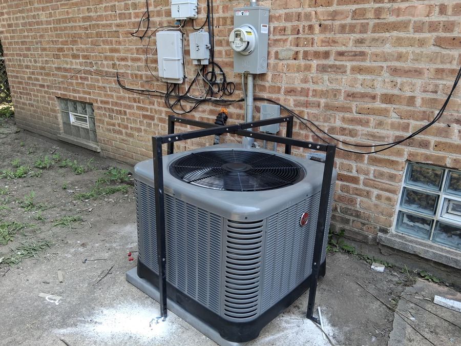 Rheem condenser mounted inside a steel protection cage against a brick wall