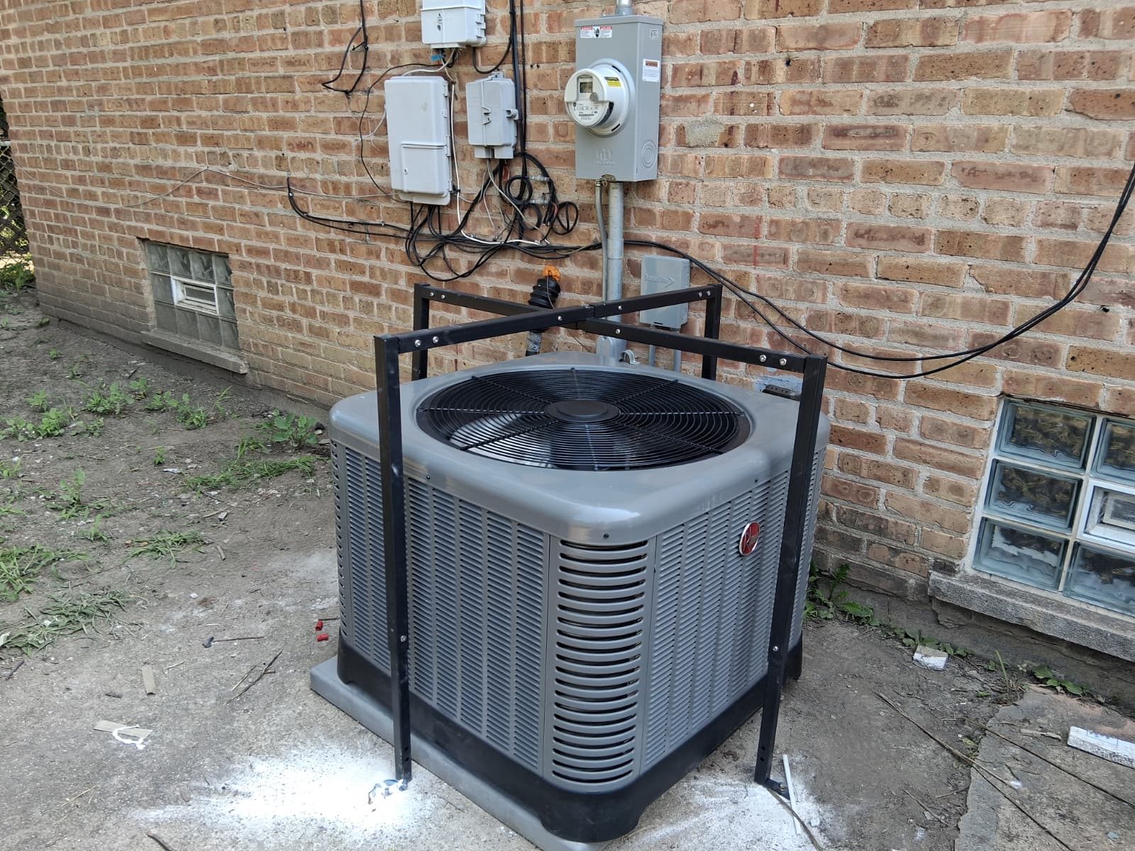 Rheem condenser installed inside a steel protection frame against a Chicago brick wall