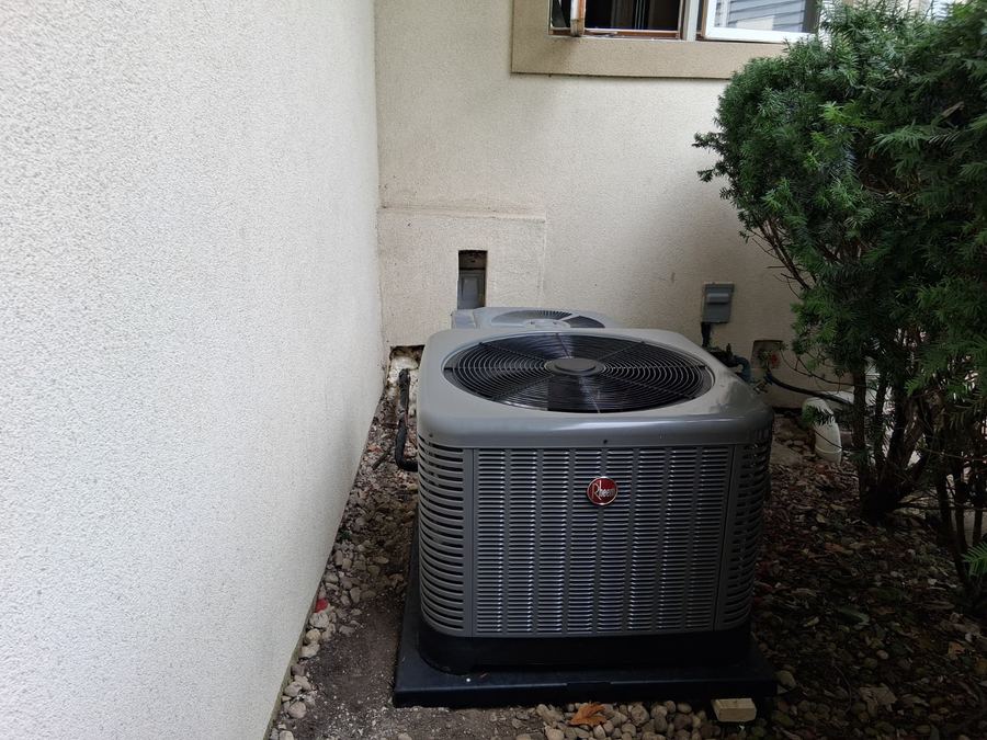 Rheem air conditioning condenser installed in a narrow side yard on a level pad