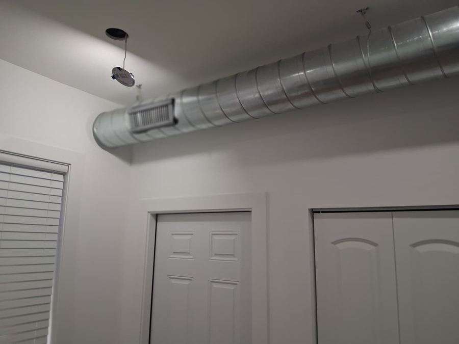 Round spiral duct run with a supply grille across a finished ceiling